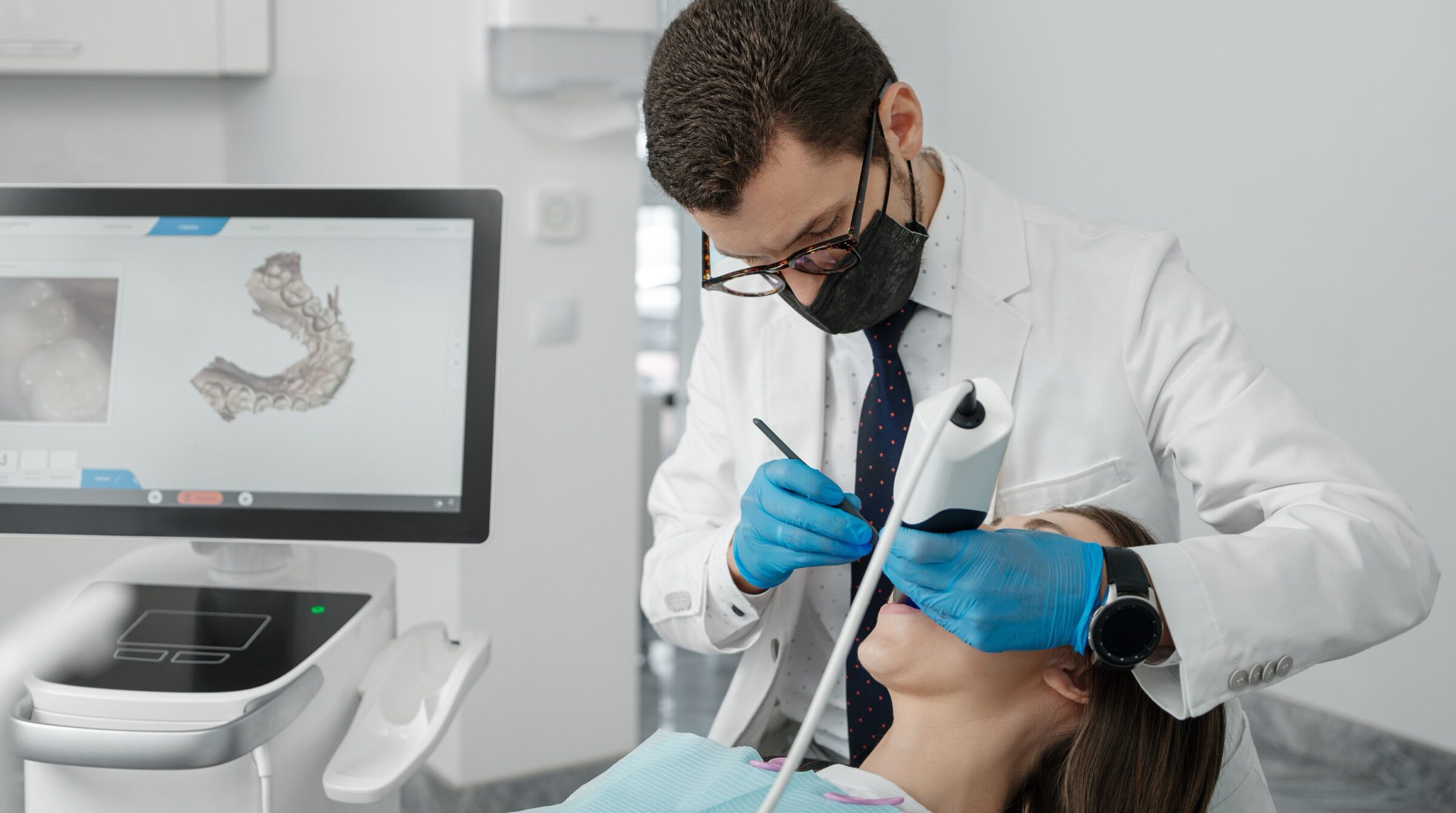 Dentist using a handheld intraoral scanner on a patient, with the 3D scan shown on a screen